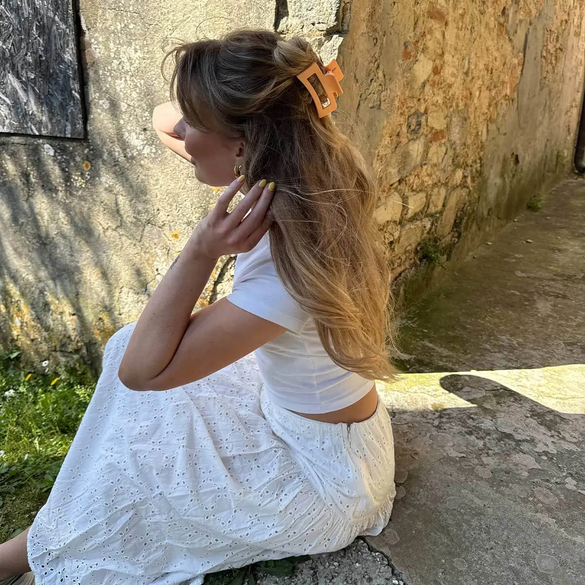 Eine Frau in einem weißen Sommer-Outfit trägt ihr Haar halb hochgesteckt mit einer orangefarbenen Haarspange.